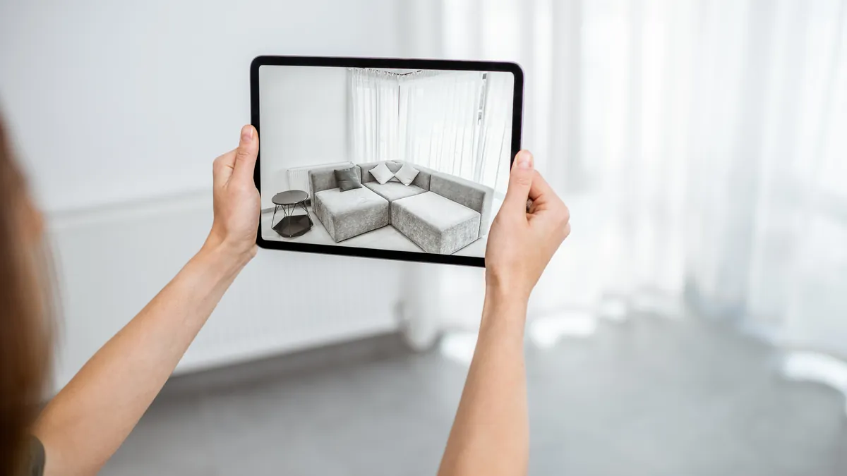 Person using an augmented reality app on a tablet to see how a sofa would look in their living room before buying it online
